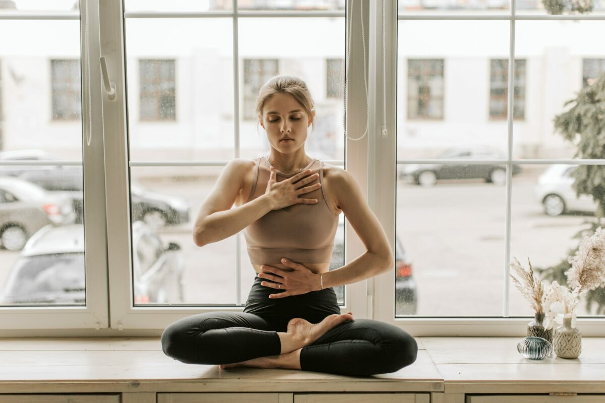 a woman sitting cross legged in front of a window in the early morning