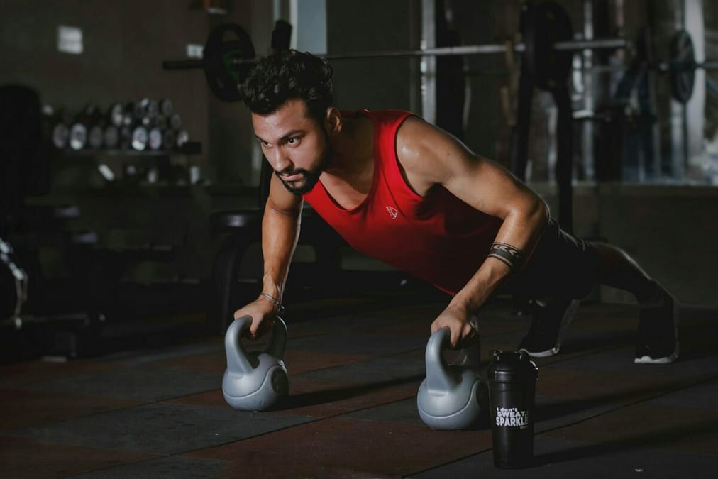 People exercising in a dimly lit gym, with water bottles and towels scattered around. The sun is setting outside, casting a warm glow through the windows