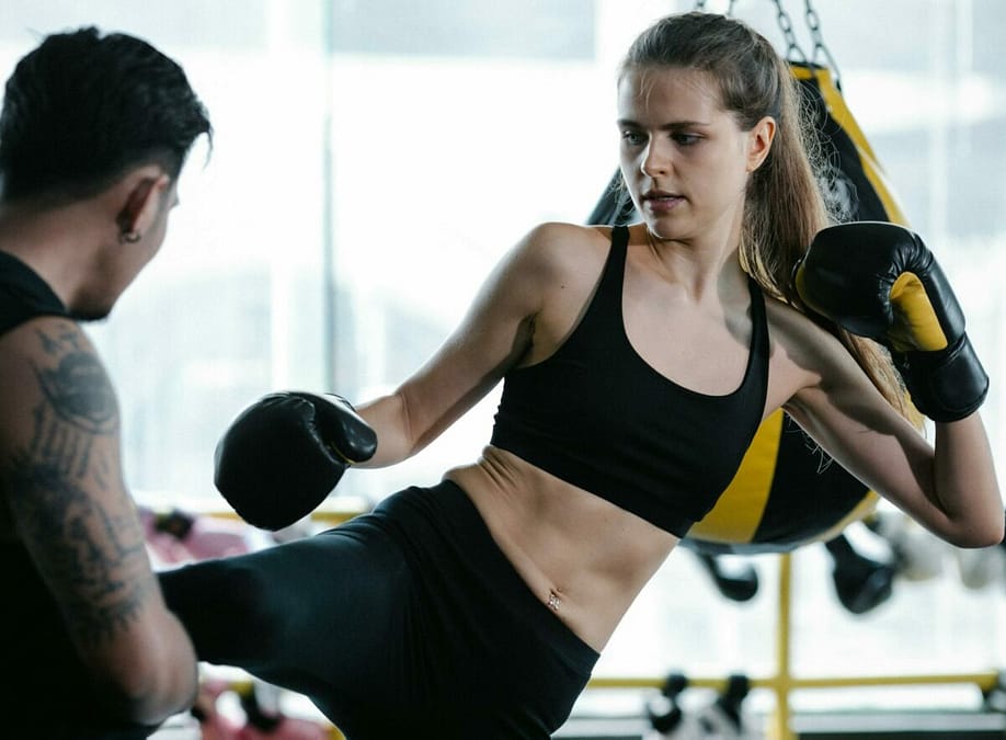 a woman kicking a man in boxing gloves