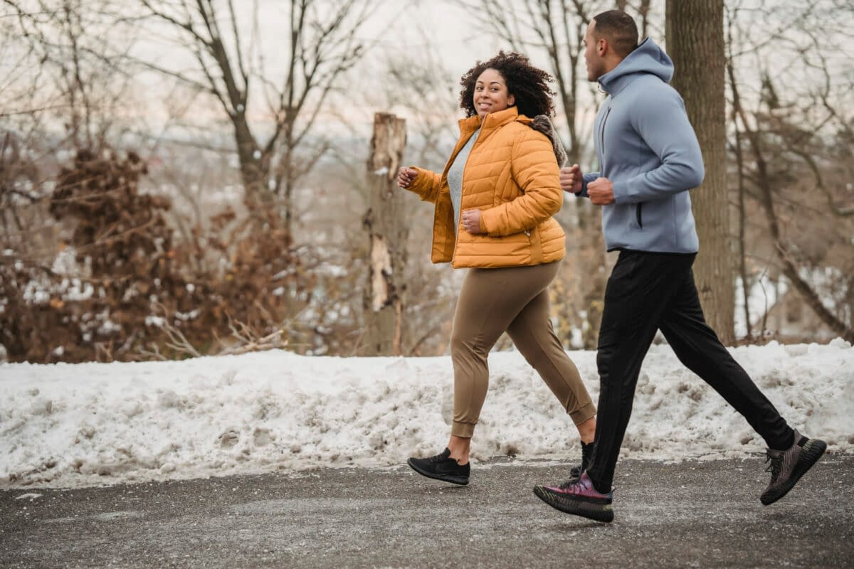 a man and woman running on a road in the snow