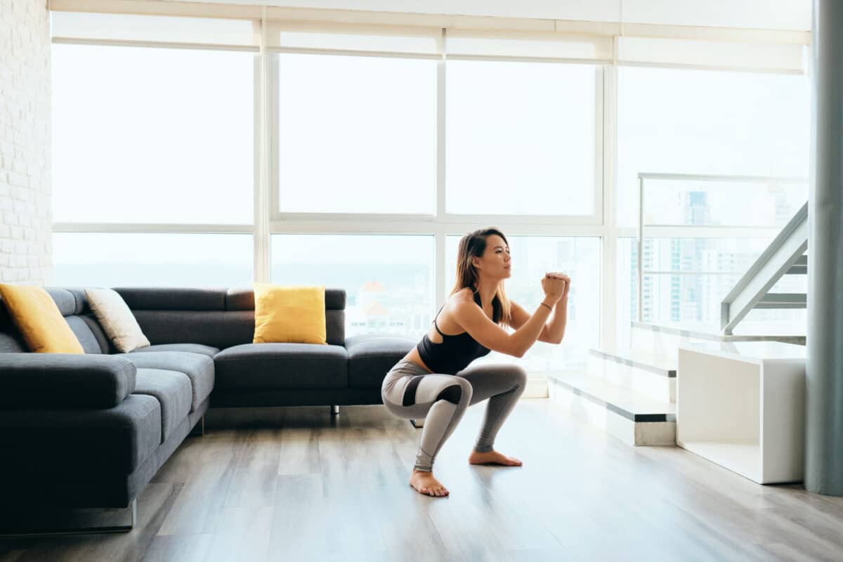 female squating in her living room during a 25 minute online training at home