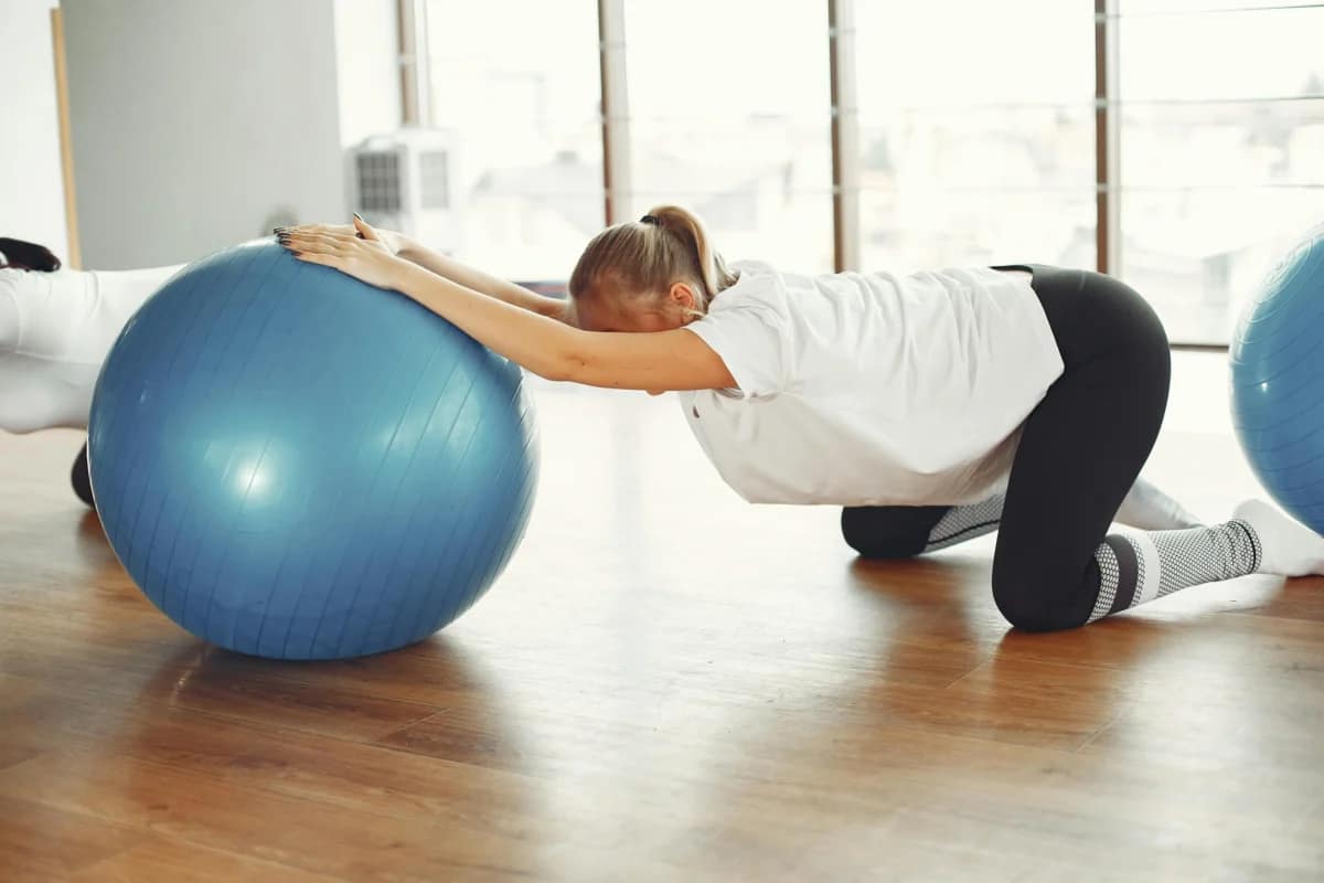 female stretching land rehabbing her lower back with a yoga ball